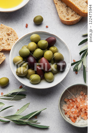 Green and black olives with olive oil, bread and himalayan pink salt on grey table 122475944