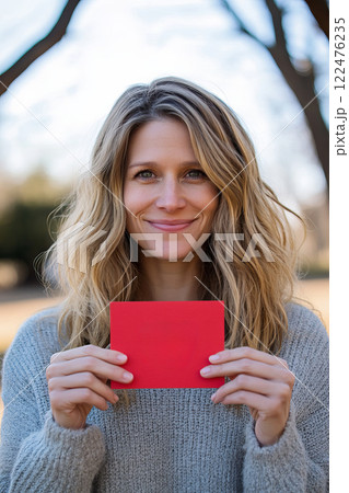 Joyful Woman Smiling While Holding Red Valentine Card in Outdoor Setting 122476235