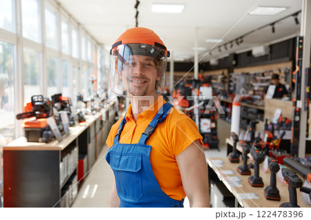 Hardware supermarket worker demonstrating modern protective helmet with visor Hardware supermarket worker demonstrating modern protective helmet with visor 122478396