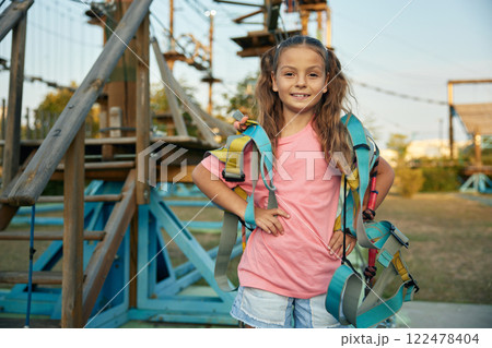 Pretty preteen girl with harness posing for camera over rope park background Pretty preteen girl with harness posing for camera over rope park background 122478404