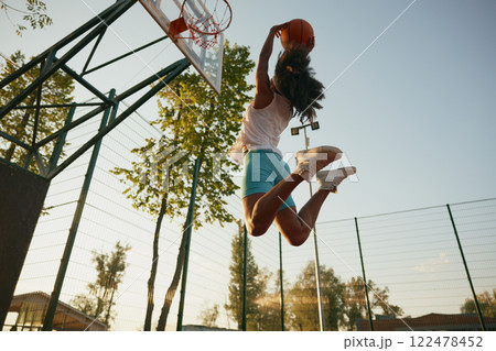 Young woman basketball player frozen in motion jumping high making slam dunk 122478452
