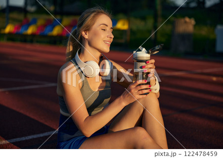 Beautiful sportswoman drinking water sitting on basketball court Beautiful sportswoman drinking water sitting on basketball court 122478459
