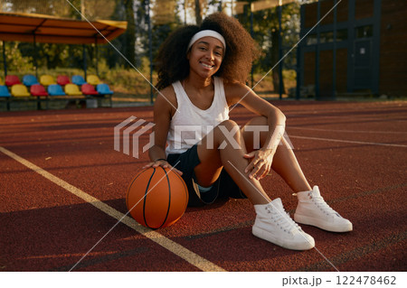 Happy relaxed teenager girl with ball sitting on basketball court 122478462