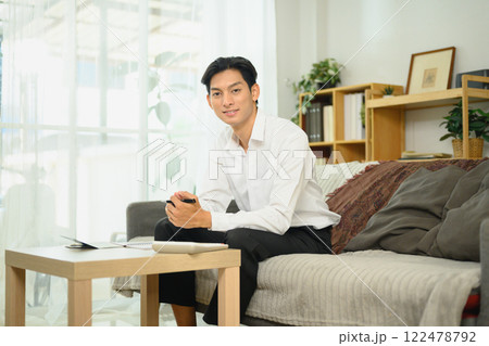 Young adult man in a white shirt sitting on couch managing his budget in a comfortable home 122478792