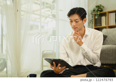Young asian man browsing or working on digital tablet in living room 122478793