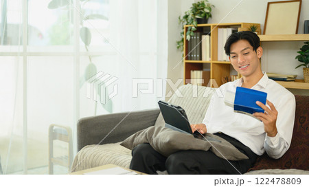 Smiling asian man holding a savings passbook and checking his financial transactions on digital tablet 122478809