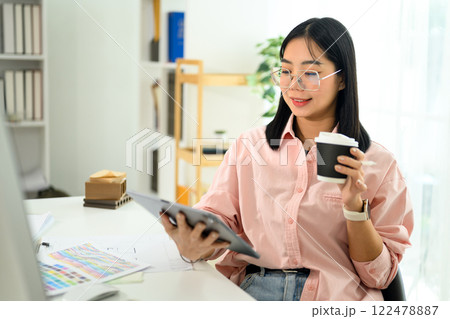 Creative interior designer enjoys a cup of coffee while reviewing design plans on digital tablet 122478887