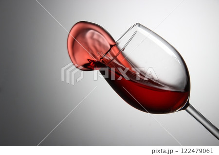 Red wine splashes elegantly from a tilted glass against a soft gray background Red wine splashes elegantly from a tilted glass against a soft gray background 122479061