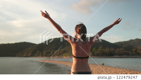 Woman in bikini is relax sandy beach of Koh Ma Beach on Koh Phangan Island in Thailand, enjoying the tropical evening sunset. Outdoor lifestyle travel on summer holiday vacation. Back view 122479247