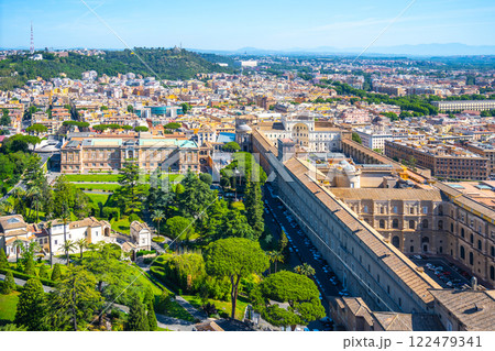 The expansive Vatican Museums and lush gardens are showcased under a clear blue sky, revealing stunning architecture and greenery amidst the backdrop of Rome's skyline. 122479341