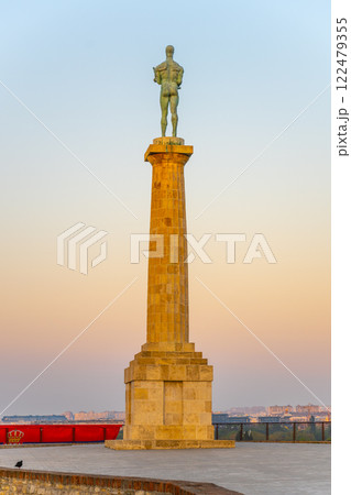 The majestic Victor Monument stands tall at Kalemegdan Fortress, silhouetted against a colorful sunset sky in Belgrade, symbolizing triumph and history at this significant location. 122479355