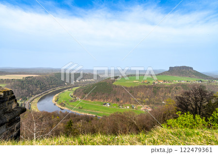 From the heights of Konigstein Fortress, the Elbe River elegantly winds through the lush Saxon landscape, showcasing verdant hills and distant cliffs under a clear sky. From the heights of Konigstein Fortress, the Elbe River elegantly winds through the lush Saxon landscape, showcasing verdant hills and distant cliffs under a clear sky. 122479361