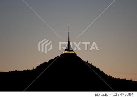 Illuminated against the twilight, Jested Tower towers over Liberec, Czechia, creating a captivating silhouette. The tranquil evening sets a peaceful atmosphere around the structure. Illuminated against the twilight, Jested Tower towers over Liberec, Czechia, creating a captivating silhouette. The tranquil evening sets a peaceful atmosphere around the structure. 122479394