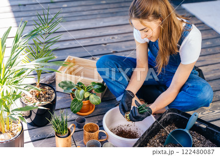 Charming woman in gloves wearing overalls, enjoy work and relax while potting plants at her backyard. Charming woman in gloves wearing overalls, enjoy work and relax while potting plants at her backyard. 122480087