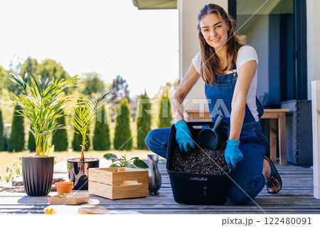 Portrait of European woman gardener in gloves wear jeans overalls with showing soil for replanting outdoor in terrace, sunny day, spring. Copy space text. 122480091