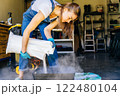 Young housewife woman in casual home clothes holds a large package holds a large package. preparing soil for plant transplantation in garage or utility room. 122480104