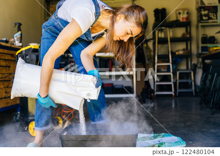 Young housewife woman in casual home clothes holds a large package holds a large package. preparing soil for plant transplantation in garage or utility room. 122480104