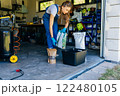 Young housewife woman in casual home clothes holds a large package holds a large package. preparing soil for plant transplantation in garage or utility room. 122480105