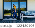 Full height woman housewife using vacuum cleaner on terrace of her house cleaning rug. 122480106