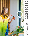 Vertical shot of woman blogger wear yellow t-shirt and overalls use ring lamp and phone, records video, how care for succulents and prepare soil for cactus replant at home in modern cozy environment. 122480112
