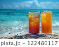 two different cocktails stand in the sand on the edge of the water on a perfect beach in the sand against the backdrop of the blue ocean. 122480117