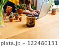 Unrecognizable young woman botanist hobbyist shopping for pots and soil for her hobby in online store at home. Close up of hands on notebook keyboard, wooden table with clay pots, plants,. 122480131