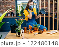 Professional lovely female gardener drinking coffee making relax pause at cozy home interior looking Internet tutorials about replanting, care of plants and gardening at home. 122480148