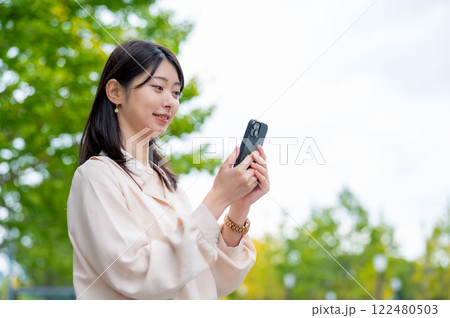 木を背景にスマホを操作する日本人女性 122480503