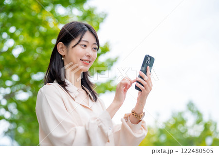 木を背景にスマホを操作する日本人女性 122480505