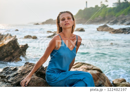 Stunning woman in wet blue dress by stormy ocean on exotic island. Model embraces beauty, femininity, nature. Sea waves crash, inspiring strength, serenity. Perfect for empowerment, freedom, fashion. Stunning woman in wet blue dress by stormy ocean on exotic island. Model embraces beauty, femininity, nature. Sea waves crash, inspiring strength, serenity. Perfect for empowerment, freedom, fashion. 122482197