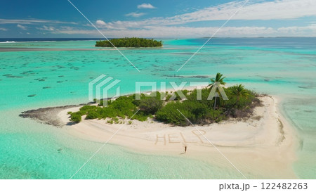 Aerial view capturing a tropical island surrounded by vibrant turquoise waters, featuring a small sandy beach where the urgent message help is written in the sand 122482263