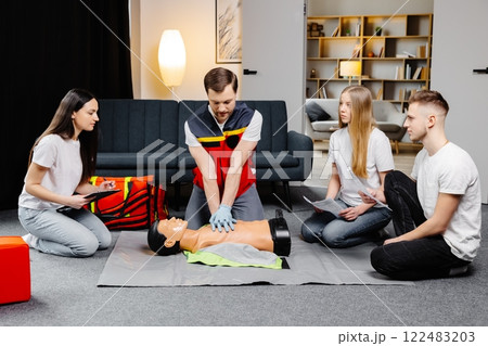 Young man instructor helping to make first aid heart compressions with dummy during the group training indoors 122483203