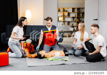Young man instructor helping to make first aid heart compressions with dummy during the group training indoors Young man instructor helping to make first aid heart compressions with dummy during the group training indoors 122483205