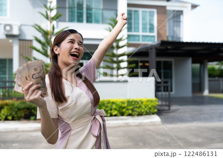 Portrait of happy attractive Asian women holding a lot of banknotes in front of home to celebrate and Pay the final installment of the house, Loans for real estate concept, Smiling young successful 122486131