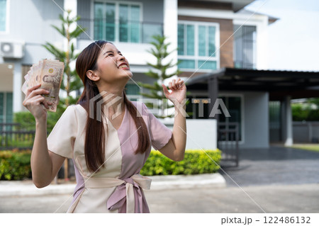 Portrait of happy attractive Asian women holding a lot of banknotes in front of home to celebrate and Pay the final installment of the house, Loans for real estate concept, Smiling young successful 122486132