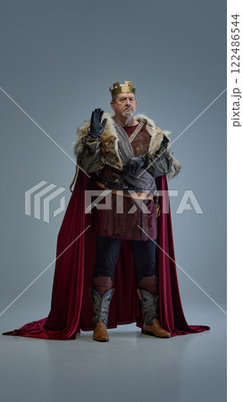 Medieval king in golden crown, fur-lined cloak, and armor, raising hand with authority. 122486544