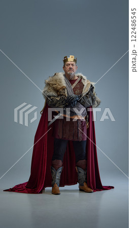 Medieval king in fur-lined cloak and golden crown, standing seriously with hands on sword. Power, authority, leadership Medieval king in fur-lined cloak and golden crown, standing seriously with hands on sword. Power, authority, leadership 122486545