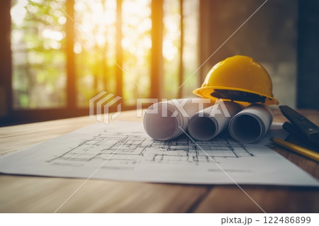 Stack of Architectural Blueprints with Yellow Hard Hat on Wooden Table in Bright Workspace 122486899