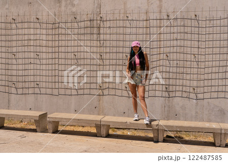 Beautiful cute smiling black hair latin woman in summer hipster casual clothes posing near wall 122487585