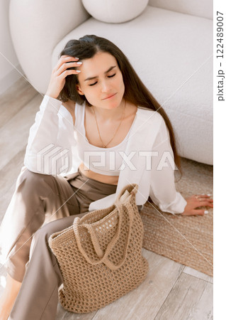 Elegant woman with long hair posing carrying a stylish woven tote bag, showcasing casual chic fashion indoors Elegant woman with long hair posing carrying a stylish woven tote bag, showcasing casual chic fashion indoors 122489007
