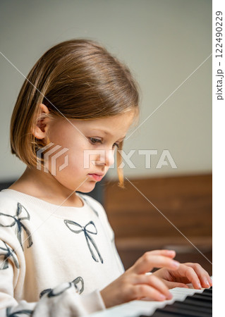 Home lesson on music for the girl on white piano synthesizer. Concept of early development: learning music enhances motor skills, hearing, and intelligence, fostering creativity from childhood 122490229