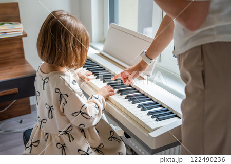 Home lesson with teacher on music for girl on white piano synthesizer. Concept of early development: learning music enhances motor skills, hearing, intelligence, fostering creativity from childhood Home lesson with teacher on music for girl on white piano synthesizer. Concept of early development: learning music enhances motor skills, hearing, intelligence, fostering creativity from childhood 122490236