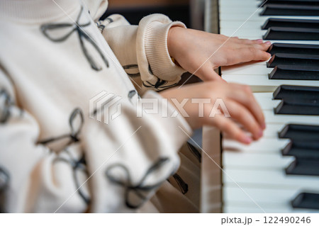 Close up view of small hands of girl on white piano synthesizer. Concept of early development: learning music enhances motor skills, hearing, and intelligence, fostering creativity from childhood 122490246