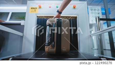 Security Check in Airport: Passenger Places Suitcase on Conveyor Belt for Baggage Screening 122490276