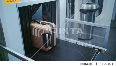 Security Checkpoint in Airport Terminal: Passenger Places Suitcase on Conveyor Belt for Baggage Screening 122490304
