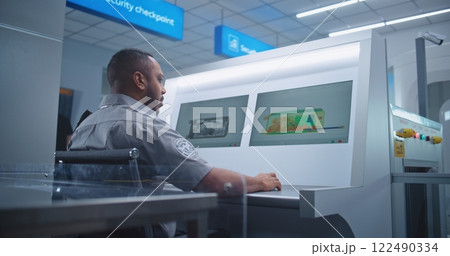 Airport Terminal: Security Officer Monitors Luggage Screening on Computer Screens, Finds Suspicious Item 122490334