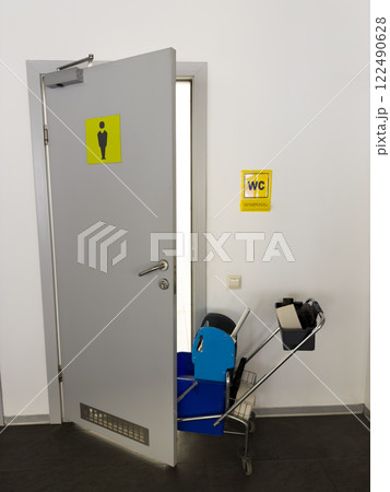 Public toilet being cleaned. Men restroom is closed while room is being cleaned using cleaning cart with supplies and new toilet paper for maintenance, vertical photo of public toilet with sign Public toilet being cleaned. Men restroom is closed while room is being cleaned using cleaning cart with supplies and new toilet paper for maintenance, vertical photo of public toilet with sign 122490628