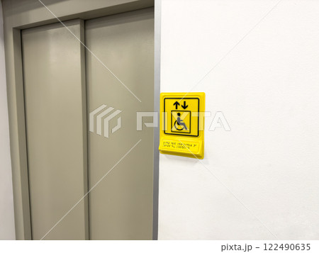 Sign near elevator doors in public place with symbol of person in wheelchair and braille text to assist in orientation for people with disabilities, care for the disabled person Sign near elevator doors in public place with symbol of person in wheelchair and braille text to assist in orientation for people with disabilities, care for the disabled person 122490635