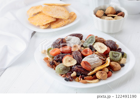 Mix of dried tropical fruits, nuts, and raisins on a white table. 122491190