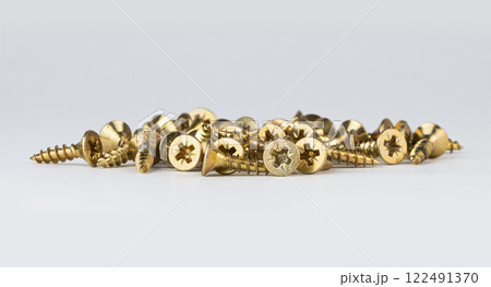 A pile of golden screws lies on a white surface ready for various projects A pile of golden screws lies on a white surface ready for various projects 122491370